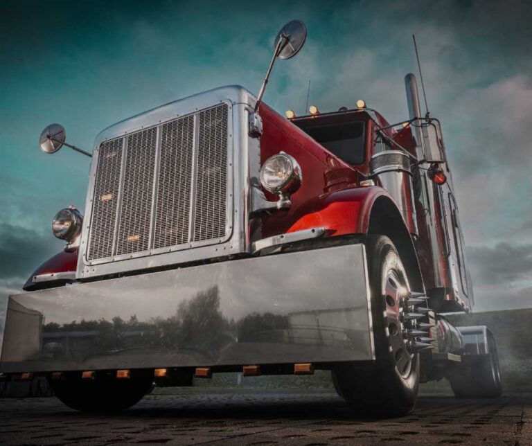 Red semi-truck with chrome details and large front grille, seen from a low angle - https://www.streetsmart.insurance/